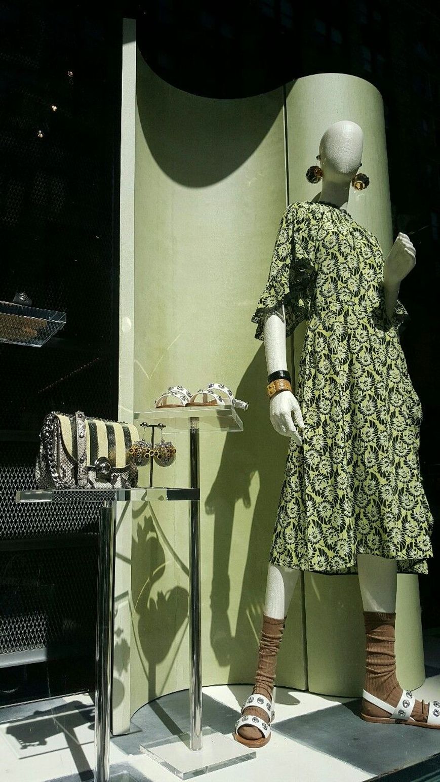 yeşil platform önünde yeşil elbise giymiş bir cansız mankenin bulunduğu butik vitrini