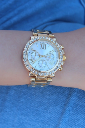 Bir model, Ebijuteri toptan giyim markasının  Gold Renk Metal Kordon Zirkon Taşlı Kasa Beyaz Kadran Romen Rakamlı Kadın Saat
 toptan Saat ürününü sergiliyor.