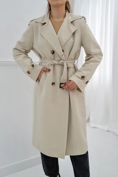 Bir model, Elisa toptan giyim markasının ELS10063 - Belted And Buttoned Trench Coat - Beige toptan Trençkot ürününü sergiliyor.