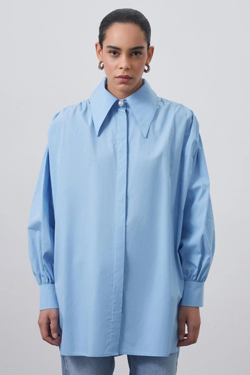 Bir model, Kadriye Baştürk toptan giyim markasının  Omuz Büzgülü Geniş Yaka Gömlek Açık Mavi
 toptan Gömlek ürününü sergiliyor.