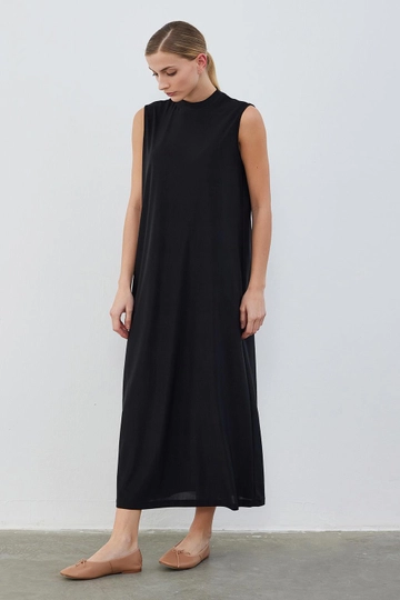 Bir model, Kadriye Baştürk toptan giyim markasının  İpek Örme Kolsuz Elbise Siyah
 toptan  ürününü sergiliyor.
