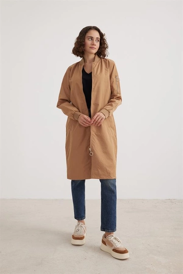 Bir model, Levure toptan giyim markasının  Paraşüt Kumaş Ribana Yaka Uzun Kol Kadın Trençkot Camel
 toptan Trençkot ürününü sergiliyor.