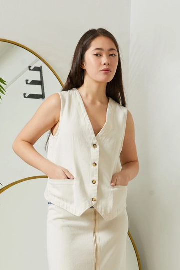 Bir model, Newgirl toptan giyim markasının  V Yaka Düğmeli Cepli Kadın Yelek - Ekru
 toptan Yelek ürününü sergiliyor.
