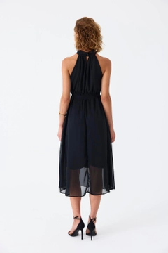 Bir model, Tuba Butik toptan giyim markasının tbu11782-halter-neck-chiffon-midi-dress-black toptan Elbise ürününü sergiliyor.